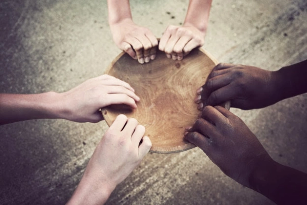 photo of three pairs of hands reaching into an empty wooden bowl